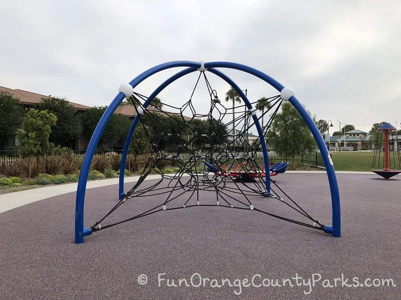 a spiderweb climber play structure with blue metal pipes curved to hold a star shaped black ropes to climb