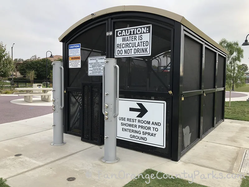 a small building that looks like a shed with metal screens around it with signs posted about how the water is recirculated and not to drink nearby two outdoor showers