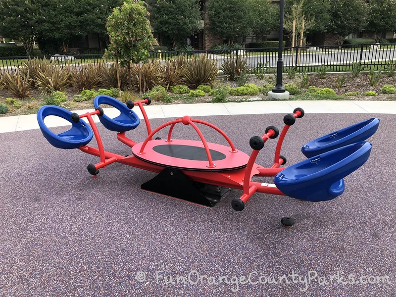 four person teeter-totter with blue seats and red handles very close to the ground