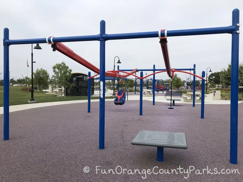 view of Veterans Sports Park at Tustin Legacy from the perspective of the zip track with a blue metal structure holding orange metal zip tracks - one with a disc seat and the other with a hanging chair
