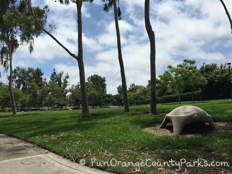 Another concrete turtle statue on the grass area with trees and a sidewalk