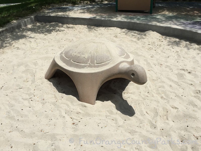 Beige concrete turtle statue for playing on in a sandbox at a Beckenham park playground