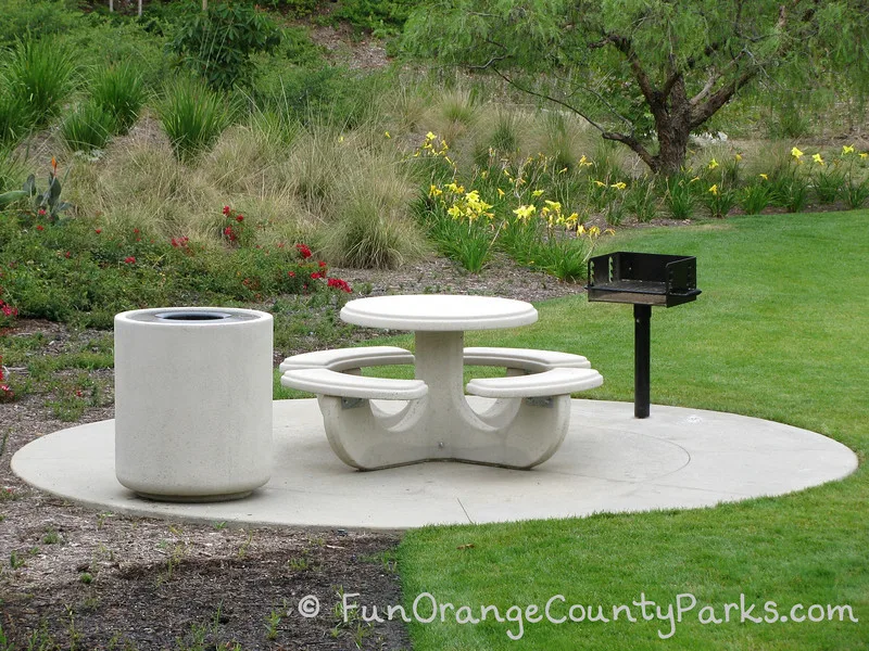 circular concrete picnic table on a concrete pad with a concrete trash receptacle and grill at Wildcatters Park in Brea