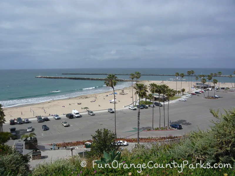 Newport Harbor entrance with two rock jetties with beach and parking lot in foreground and palm trees