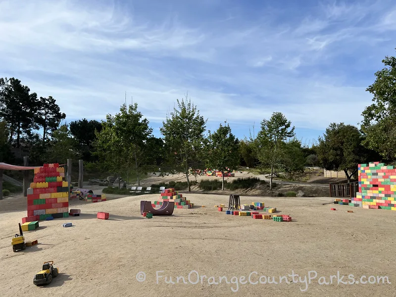 colorful large lego style blocks on a dirt surface with trees and blue sky 