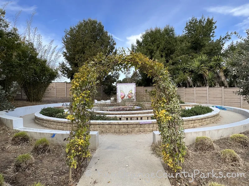 ivy arch into the sensory garden which is a spiral shape with concrete blocks marking the path - a colorful butterfly marks the doors of a storage unit