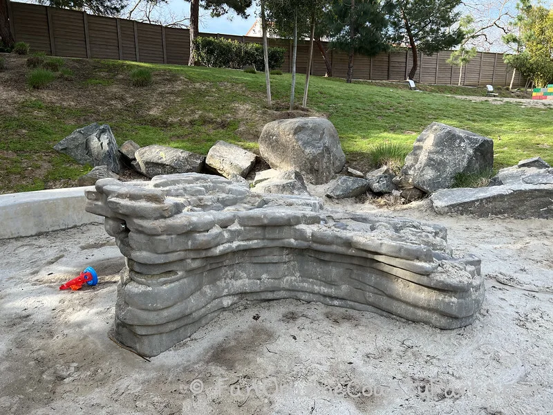 gray stones and water feature with sand for making dams and playing in the water near a green grassy hill