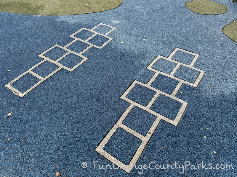 white outlined hopscotch grids inside blue recycled rubber playground surfacing at Knotty Pine Park in Laguna Hills