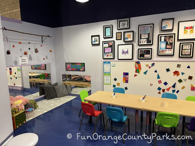 clean table with small colorful chairs and artwork hanging on the walls plus a child seating area on the floor with carpet, pillows, and mirrors on the wall